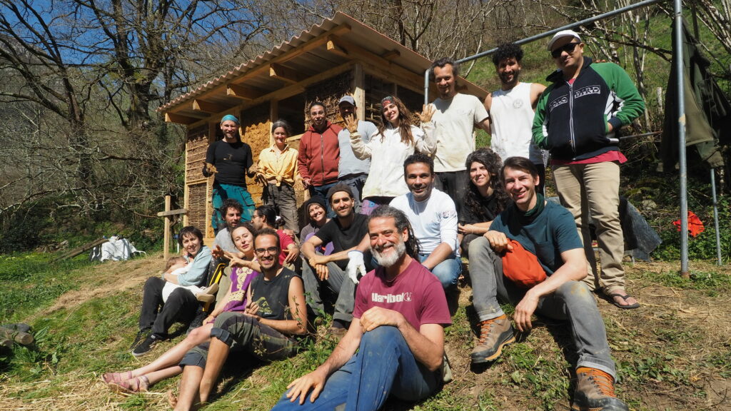Participants pose in front of the natural building structure they built together during the Clay and Straw as a Key project.