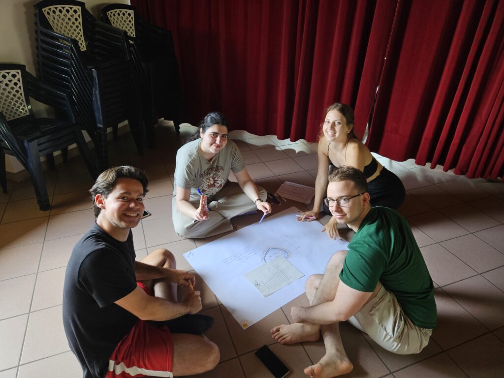 Four young people working together on a creative activity around a large sheet of paper during a youth exchange workshop.